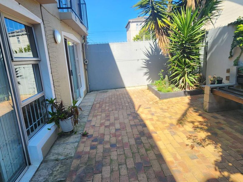 A private rear courtyard featuring brick paving, a raised planter box, and direct access to the apartment through sliding glass doors.