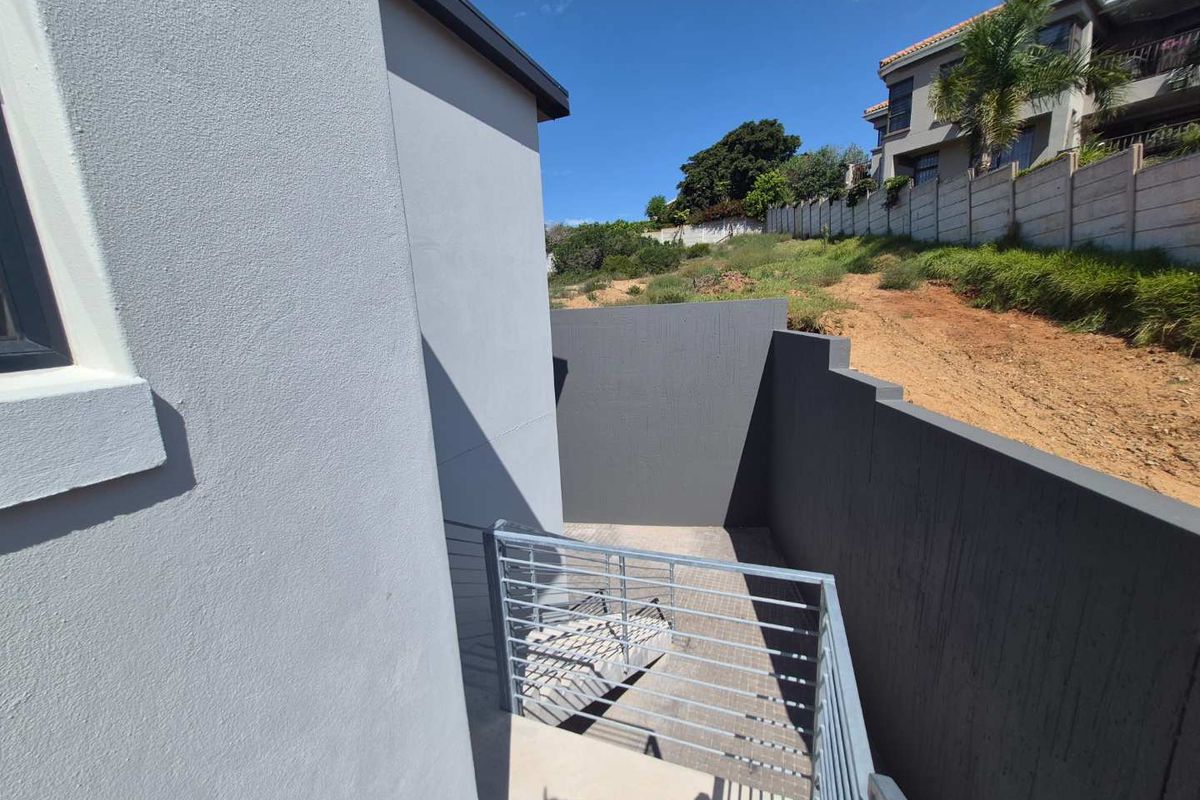 An exterior view of a paved side courtyard area featuring modern grey boundary walls and a metal staircase with horizontal railing.