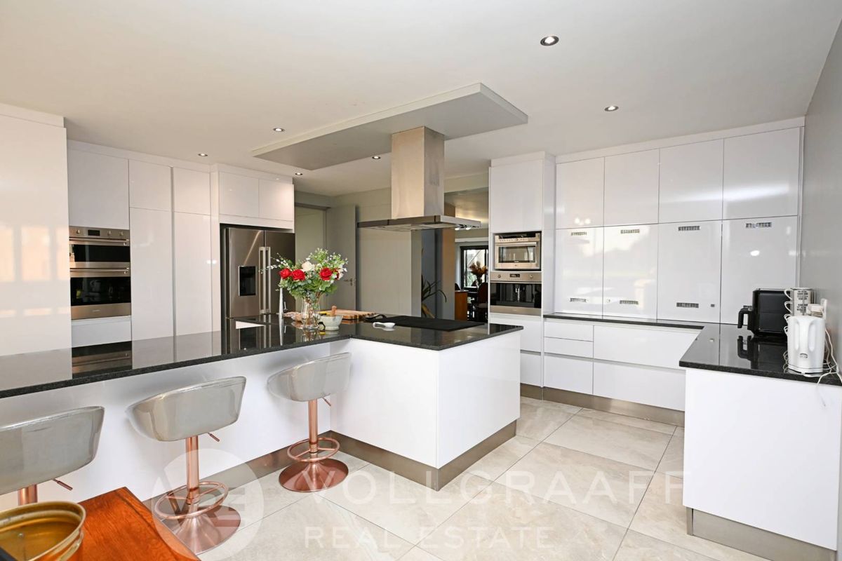 Modern kitchen featuring high-gloss white cabinetry, black granite countertops, a central island with breakfast bar, and integrated stainless steel appliances.