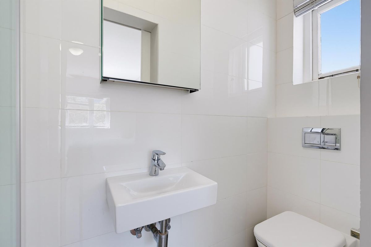 A clean, modern bathroom featuring a wall-mounted basin, chrome fixtures, a wall-hung toilet, and white tiled walls.