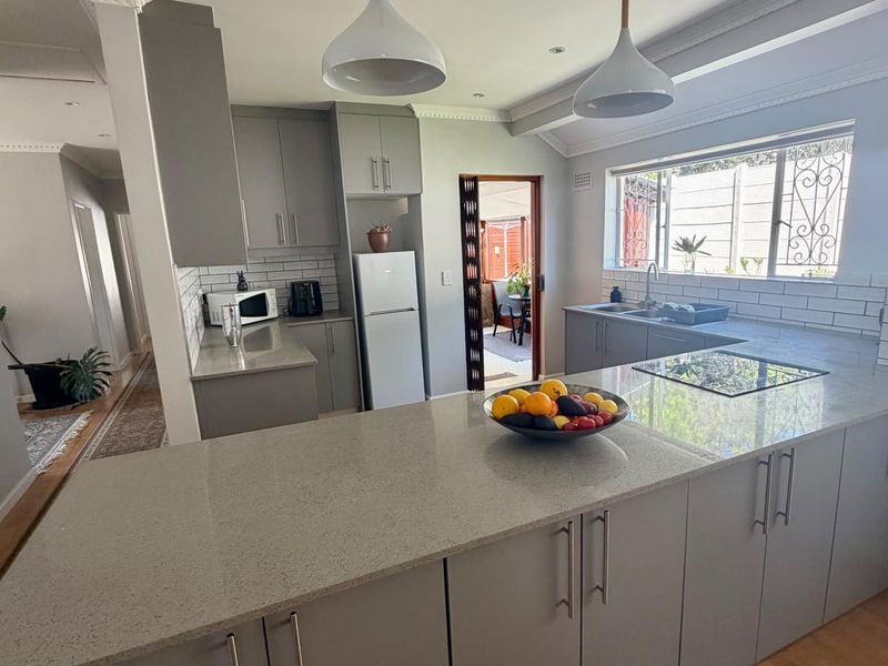 Modern kitchen featuring grey cabinetry, quartz countertops, subway tile backsplash, and a functional island layout with integrated cooktop and ample storage.
