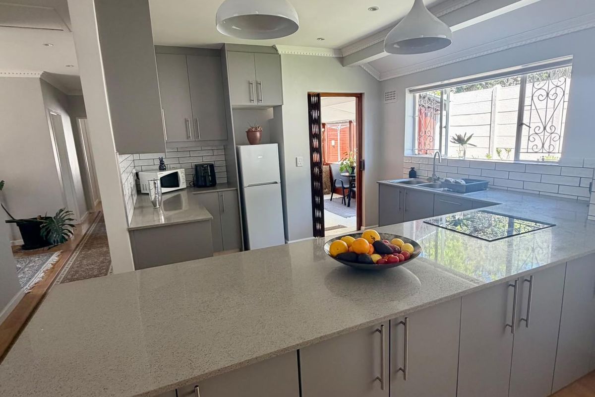 Modern kitchen featuring grey cabinetry, quartz countertops, subway tile backsplash, and a functional island layout with integrated cooktop and ample storage.