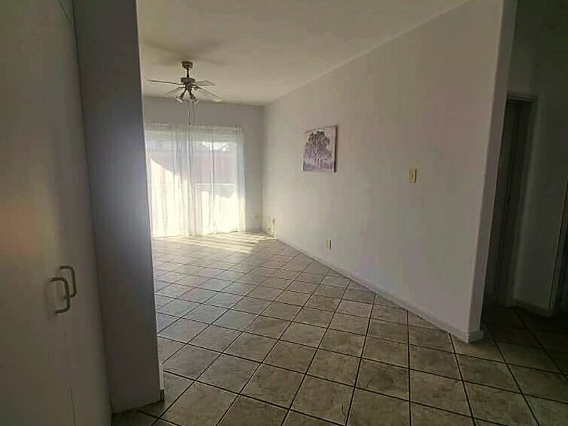 An open-plan living area featuring neutral tiled flooring, a ceiling fan, and a sliding glass door providing access to the exterior.