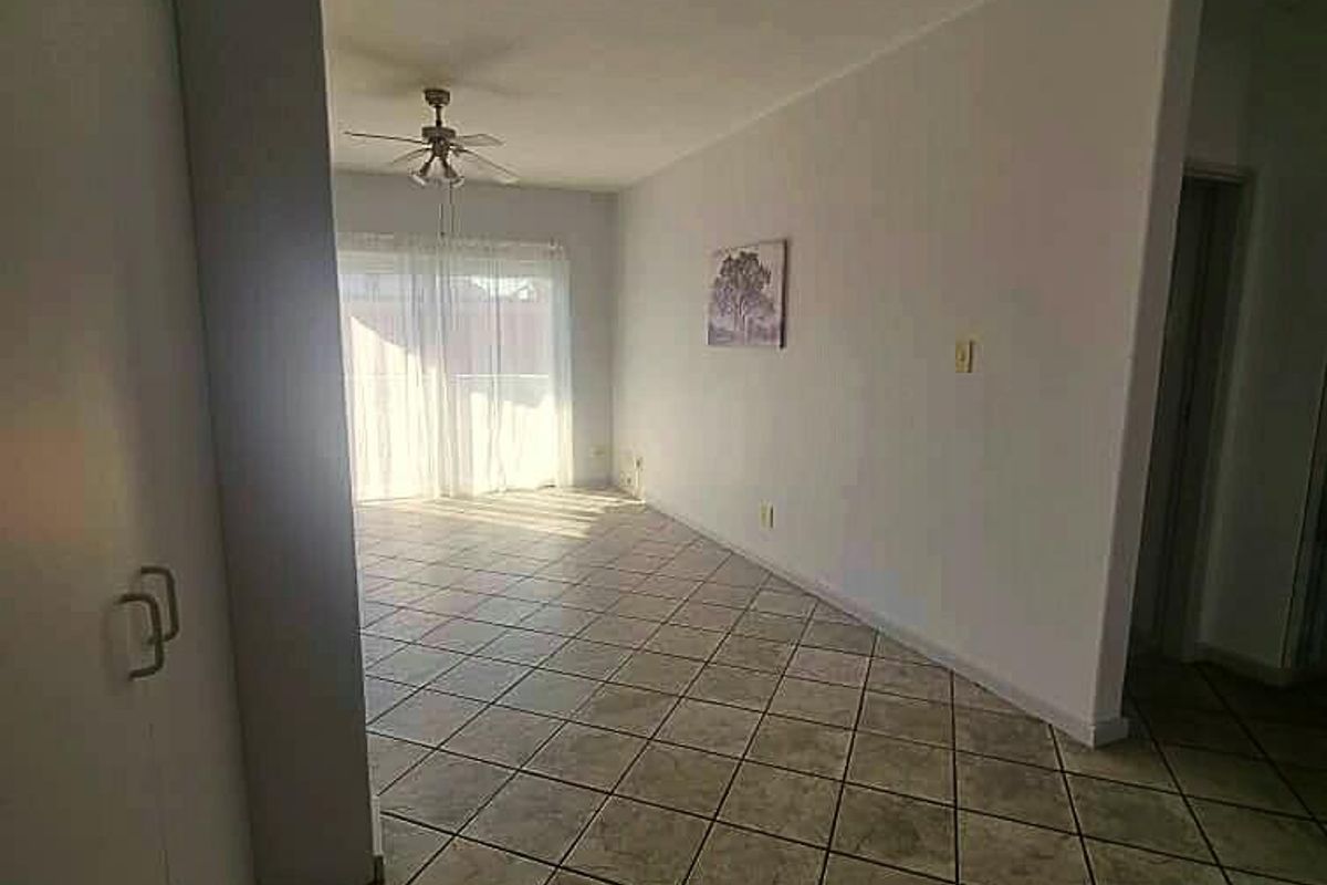 An open-plan living area featuring neutral tiled flooring, a ceiling fan, and a sliding glass door providing access to the exterior.