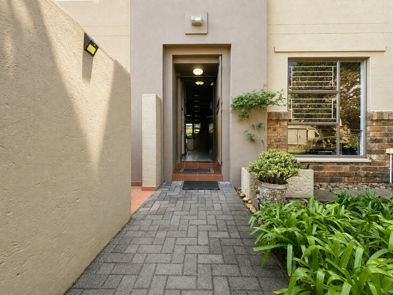 A well-maintained front entrance of a townhouse featuring a paved walkway, secure entry door, and neat brick and plaster facade detailing.