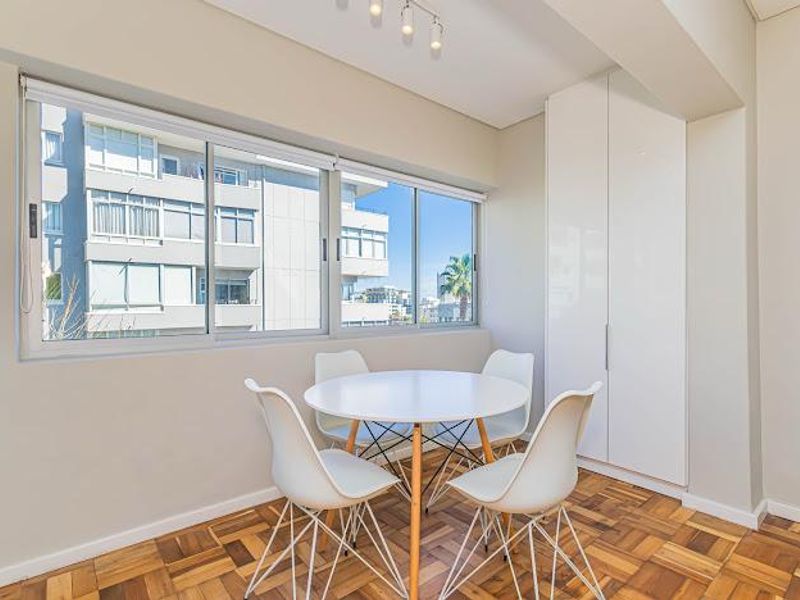 A bright dining area featuring polished parquet flooring, a large sliding window, and a sleek, full-height built-in storage cupboard.