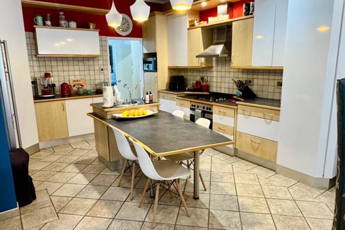 Spacious kitchen featuring a central island with integrated dining, light wood cabinetry, tiled backsplash, and modern pendant lighting.