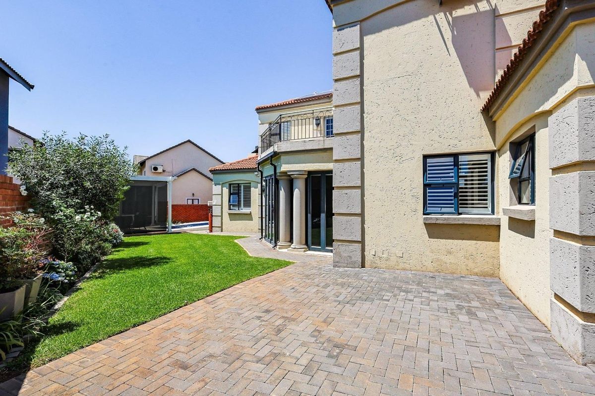 A well-maintained rear exterior view featuring a paved patio area, landscaped lawn, and a balcony overlooking the garden space.