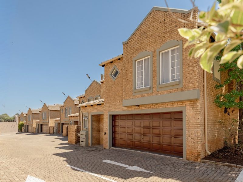 A well-maintained townhouse complex featuring face brick facades, paved driveways, and secure sectional garage doors under a clear blue sky.