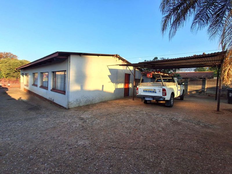 Exterior view of the property featuring a side carport, gravel and concrete driveway, and a single-story building structure with metal roofing.