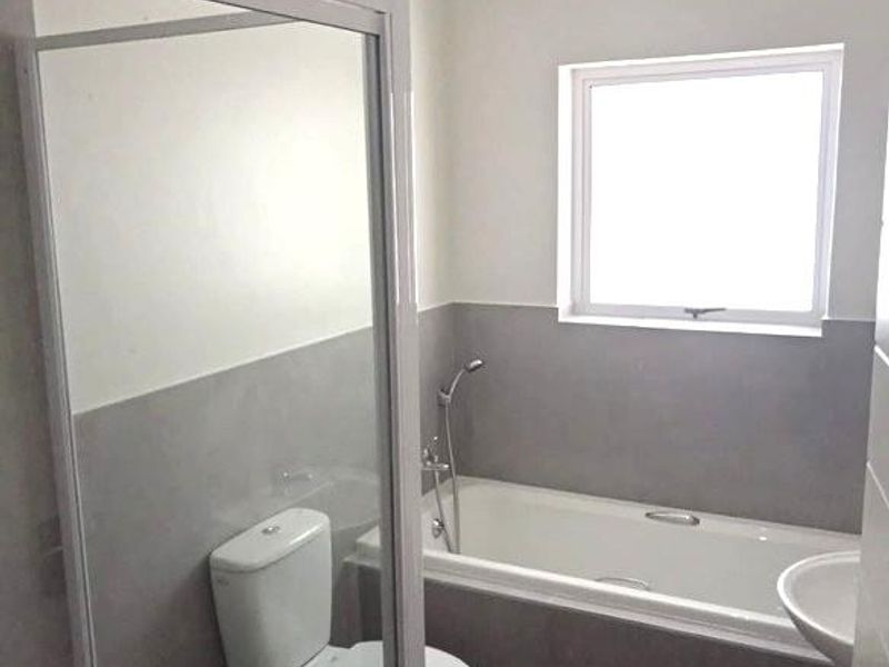 A clean, modern bathroom featuring a shower enclosure, bathtub, toilet, and washbasin with neutral grey wall and floor tiling.