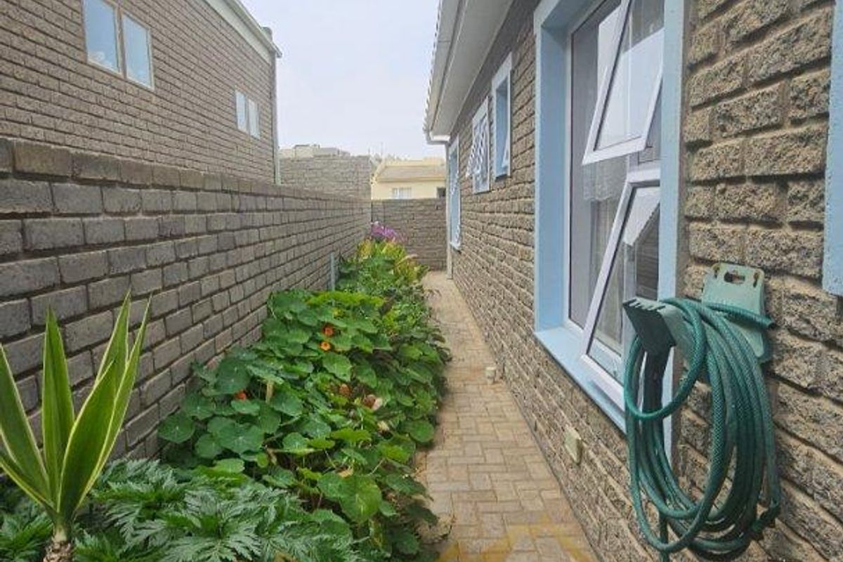 A side exterior walkway featuring brick paving, a brick boundary wall, and a garden bed along the side of the house.
