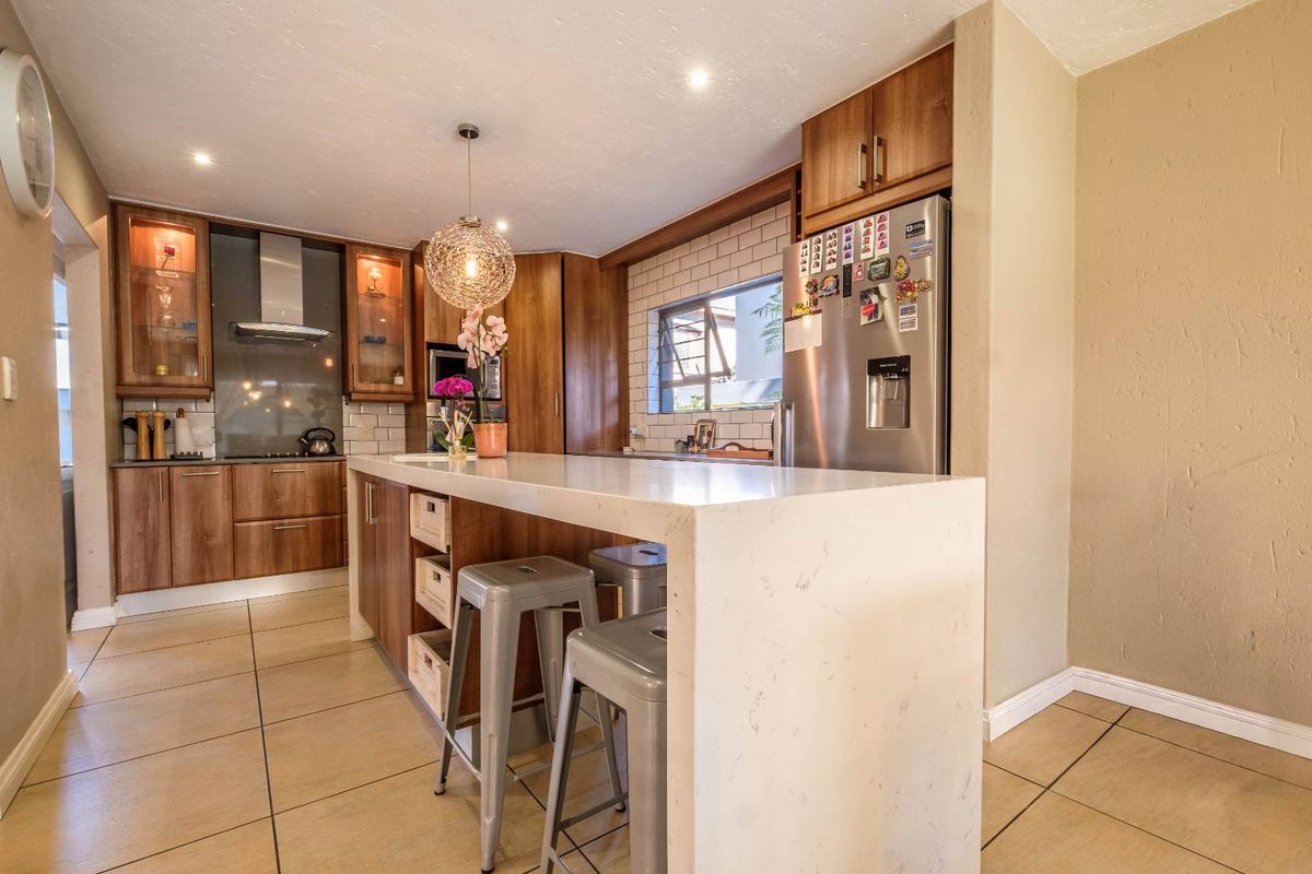 Modern kitchen featuring wooden cabinetry, a stone-topped island, tiled backsplash, and recessed lighting, creating a functional and stylish culinary space.