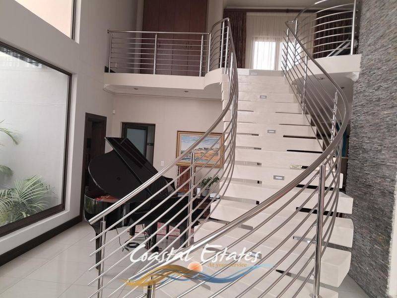 Grand entrance hall featuring a striking curved staircase with stainless steel balustrades, recessed lighting, and a textured stone feature wall.