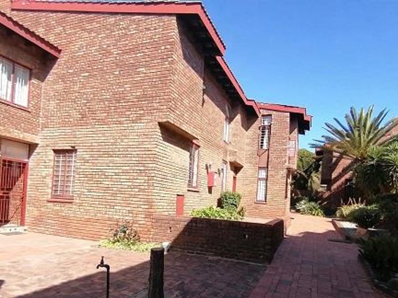 A view of the rear exterior of the townhouse featuring a face brick facade, paved courtyard area, and established garden landscaping.