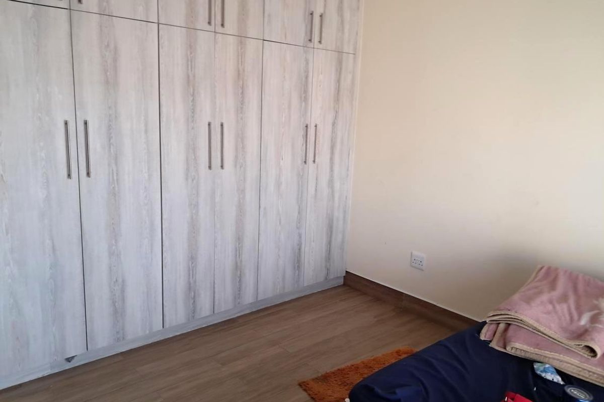 A bedroom featuring light wood-grain built-in cupboards and modern laminate flooring, providing ample storage and a clean, neutral aesthetic.