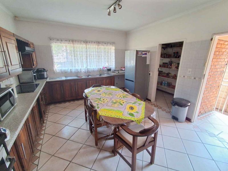 A functional kitchen featuring wooden cabinetry, laminate countertops, a double basin sink, and an adjoining walk-in pantry with tiled flooring throughout.