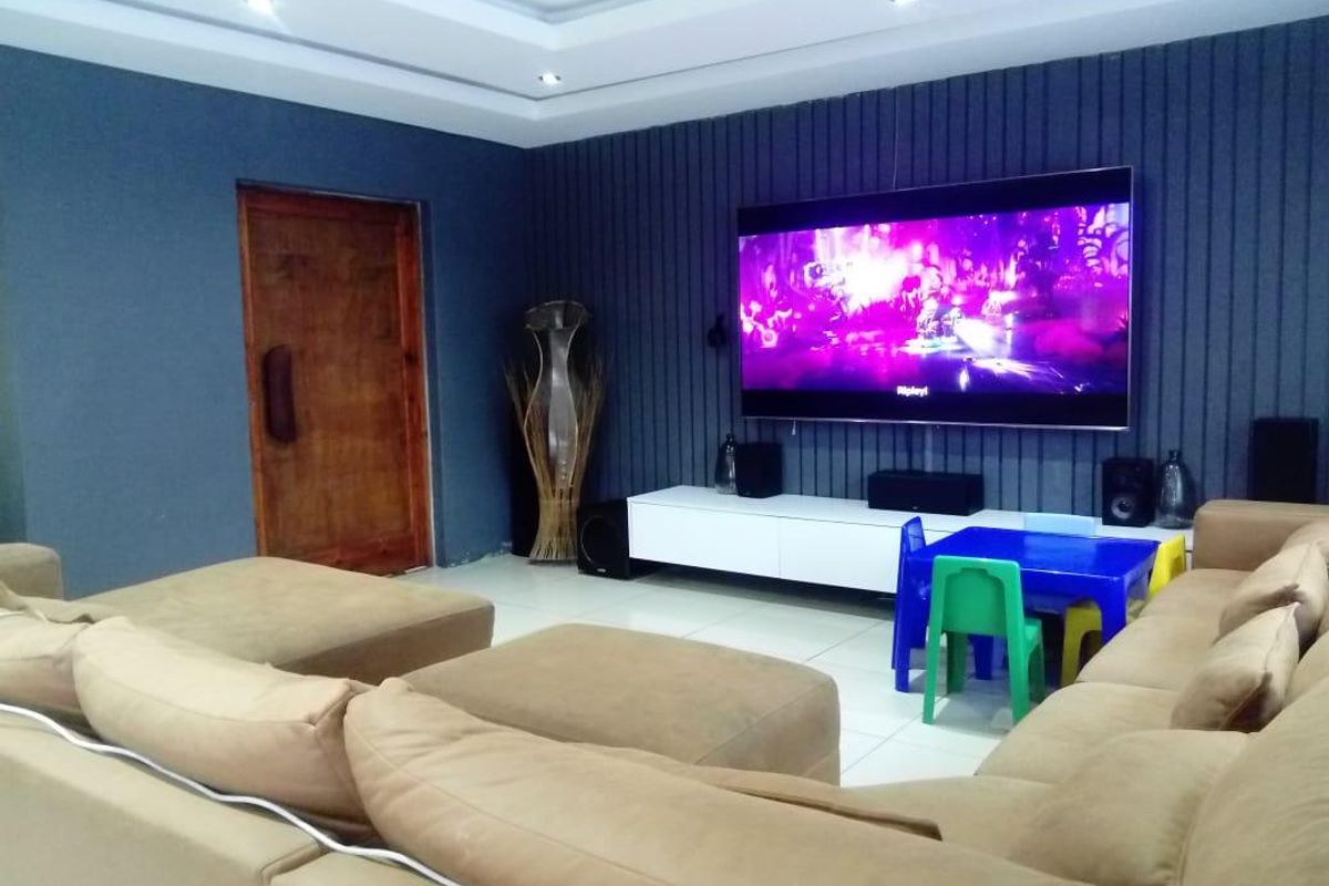 Spacious living room featuring a modern dark-toned feature wall with integrated media setup, recessed ceiling lighting, and large format floor tiles.