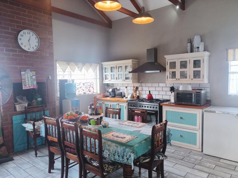 Open-plan kitchen and dining area featuring exposed timber beams, a brick fireplace, and custom cabinetry with timber countertops.