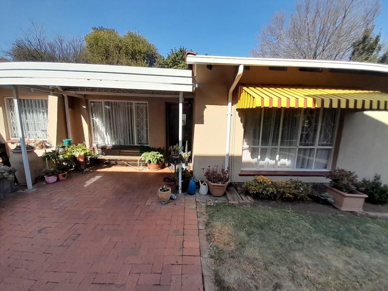 Front exterior view of the house featuring a brick paved driveway, covered carport area, and window awnings.