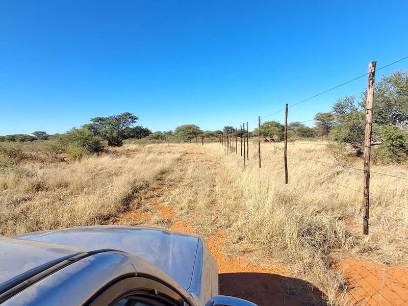 A view of the farm property boundary featuring a wire fence with wooden posts running along the edge of the veld.