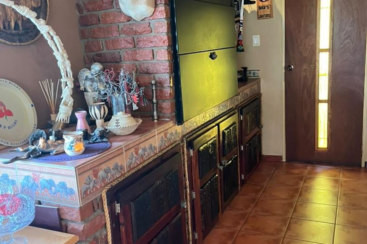 A living area featuring a prominent brick fireplace with built-in cabinetry, tiled flooring, and a timber-clad ceiling.