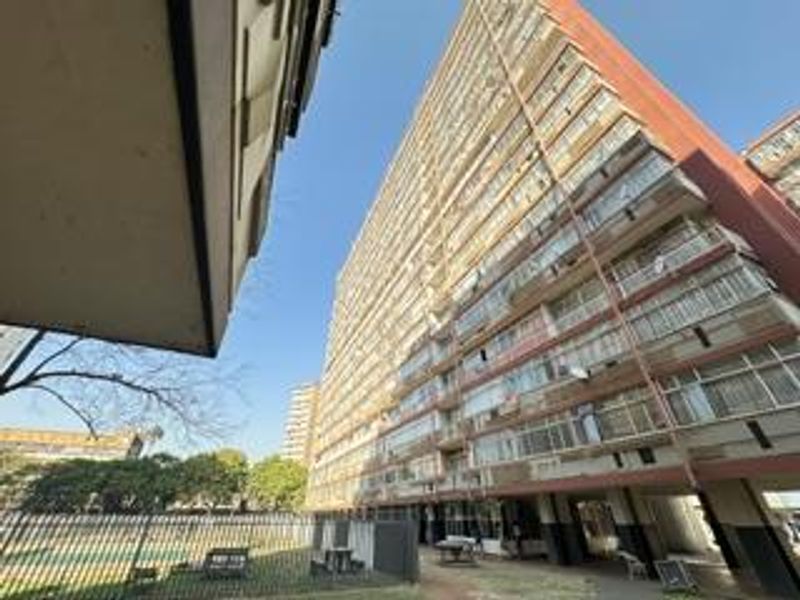 Exterior view of a multi-story apartment building featuring a large facade with multiple balconies and ground-level security fencing.