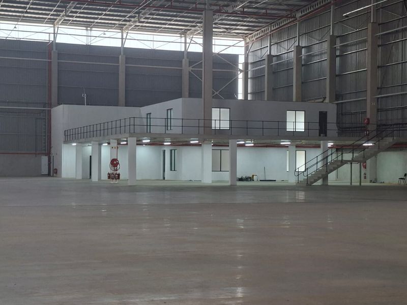 Large industrial warehouse space featuring a mezzanine level with office or storage areas, concrete flooring, and high-clearance metal structure.