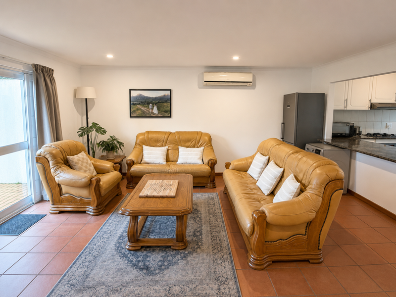 Open-plan living area featuring tiled floors, air conditioning, and a connected kitchen with granite countertops and built-in appliances, leading to an outdoor patio.