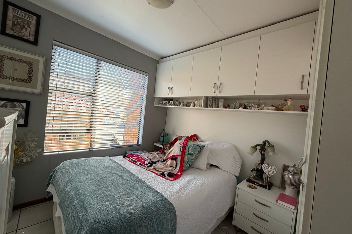 A compact bedroom featuring built-in overhead storage cabinetry, tiled flooring, and a window fitted with venetian blinds.