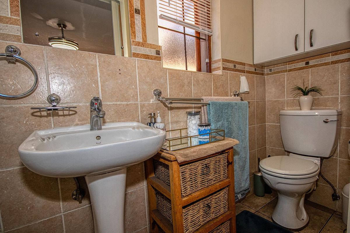 A compact bathroom featuring a pedestal basin, a standard toilet, and tiled walls with a window for natural light.