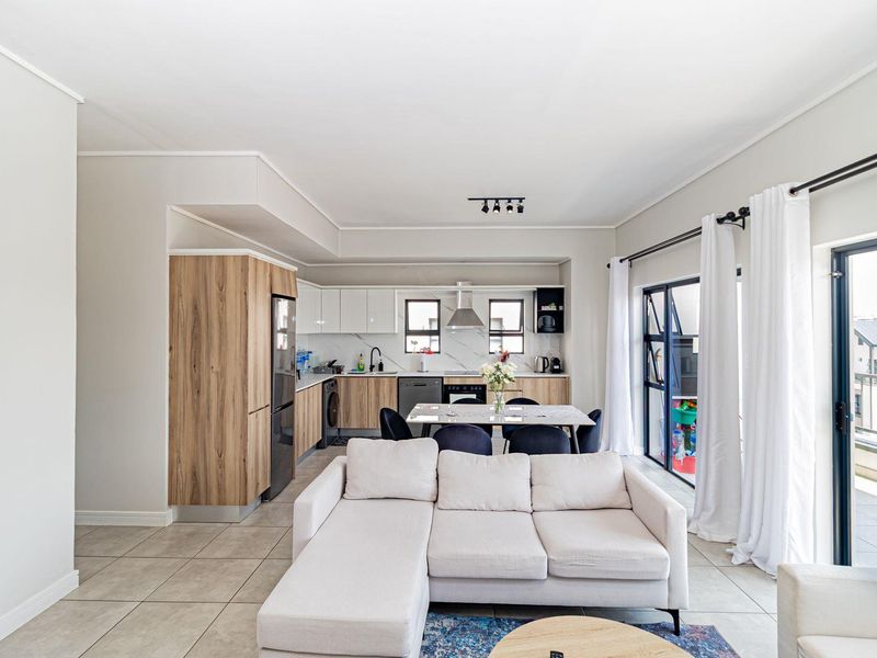 Modern open-plan living area featuring a contemporary kitchen with wood-grain cabinetry, tiled floors, and direct access to a private balcony.