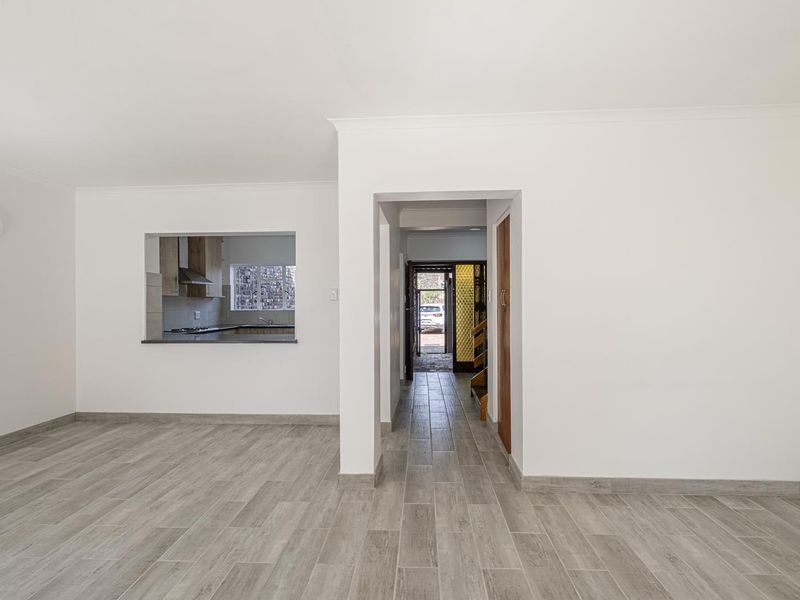 A bright, empty living area featuring modern wood-look tile flooring, coving, and a convenient pass-through window connecting to the kitchen space.