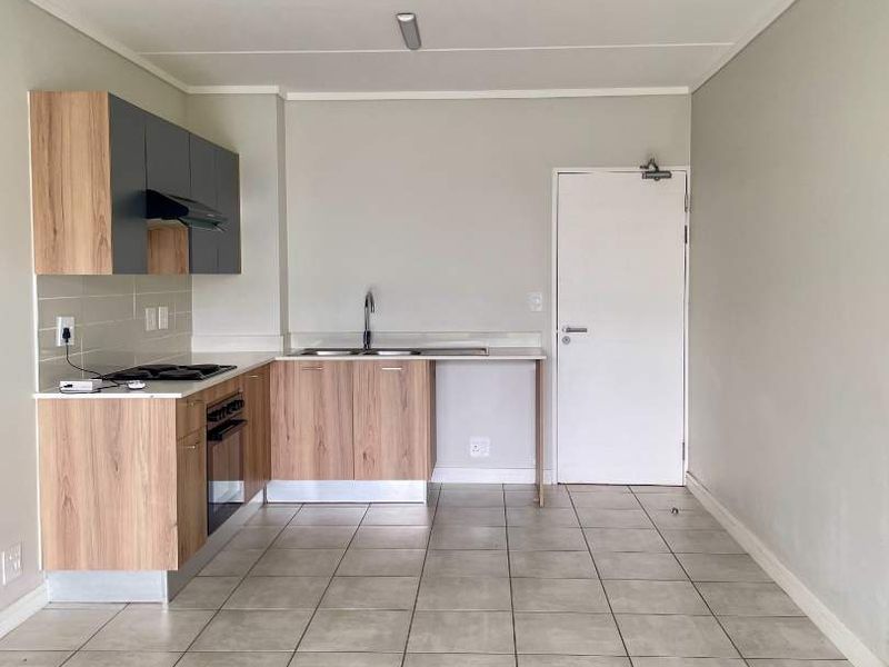 A clean, modern kitchen featuring light wood-tone cabinetry, dark grey upper cabinets, integrated appliances, and neutral tiled flooring in an open-plan layout.