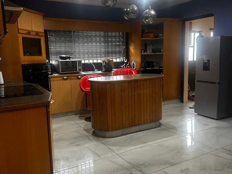 A functional kitchen featuring wooden cabinetry, a central island, built-in oven, extractor fan, and polished tiled flooring with modern recessed lighting.