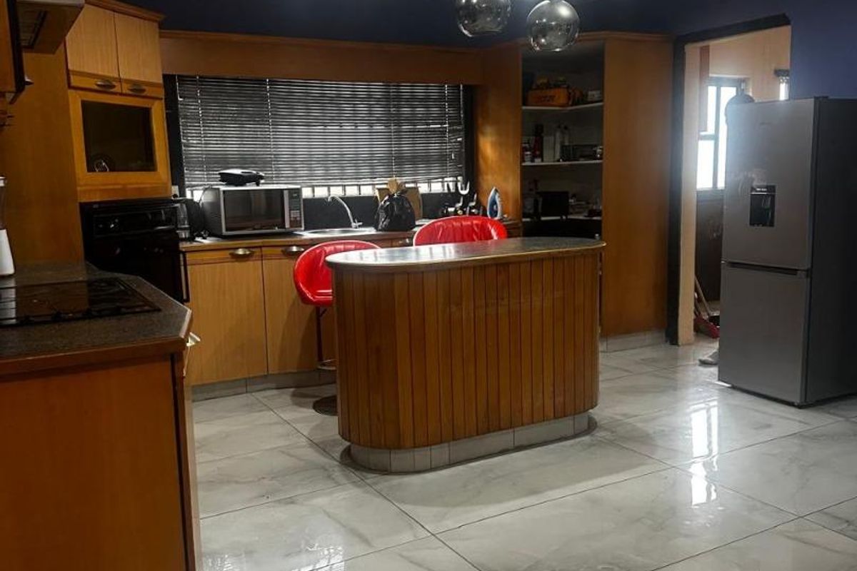 A functional kitchen featuring wooden cabinetry, a central island, built-in oven, extractor fan, and polished tiled flooring with modern recessed lighting.