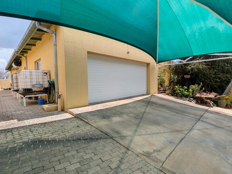 Exterior view of a garage with a paved driveway, shade sail covering, and a rainwater storage tank installed alongside the building.