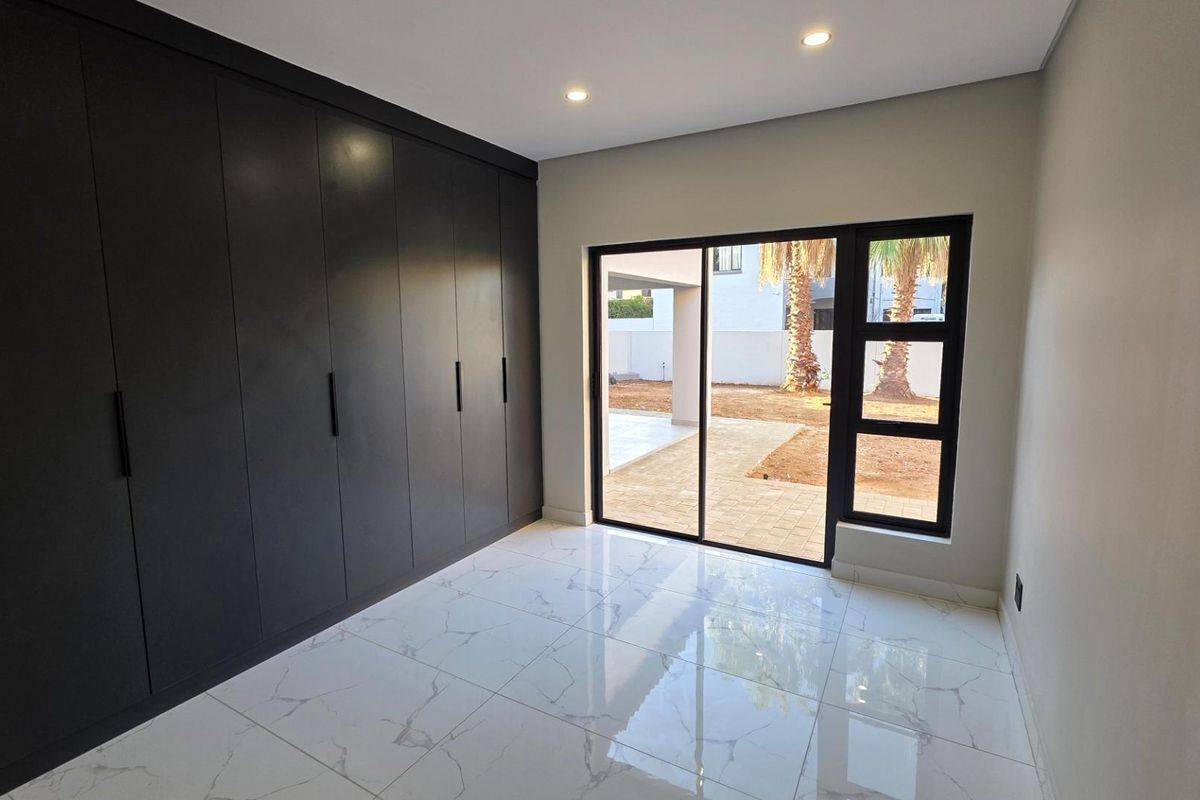 A modern bedroom featuring sleek floor-to-ceiling built-in cupboards, polished marble-look floor tiles, and sliding glass doors opening to an outdoor patio area.