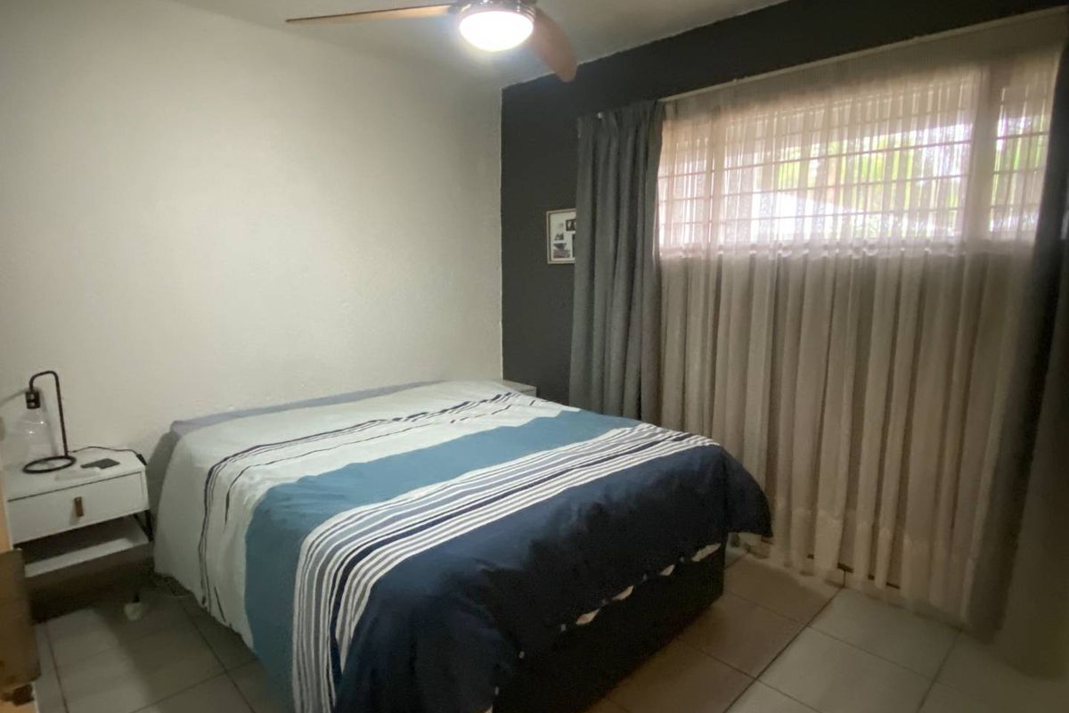 A bedroom featuring tiled flooring, a ceiling fan, and a window with security bars.