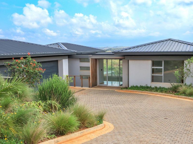 Modern single-story residence featuring a paved driveway, metal roofing, and a glass-paneled entrance, set within a landscaped environment.