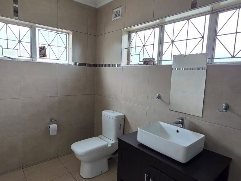 A functional bathroom featuring neutral wall and floor tiling, a modern vessel sink on a vanity cabinet, and security bars on the windows.