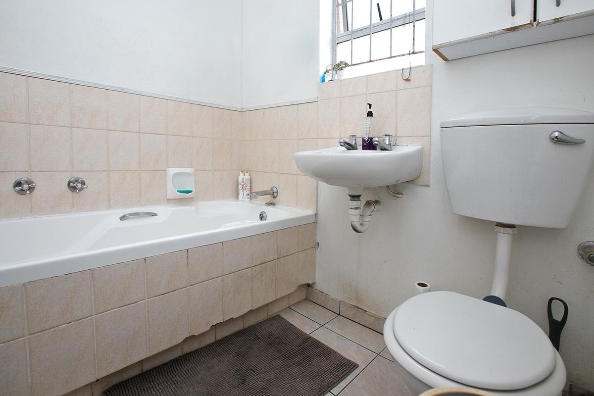 A dated bathroom featuring a standard bathtub, wall-mounted basin, and toilet with tiled splashbacks and a security-barred window.