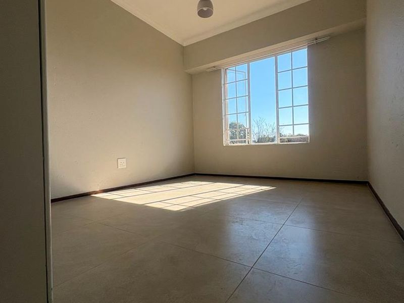 A bright, empty bedroom featuring neutral tiled flooring, a modern pendant light fixture, and a large grid-pattern window allowing for ample natural light.