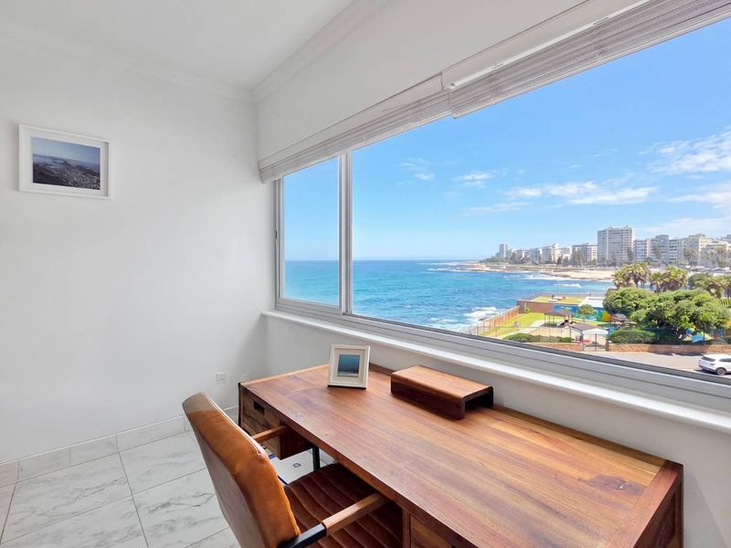 A bright office space featuring large windows with expansive ocean and coastal views, complemented by modern marble-look flooring.