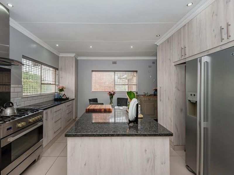 Modern kitchen featuring a central island with granite countertops, light wood-finish cabinetry, stainless steel gas stove, and recessed lighting.