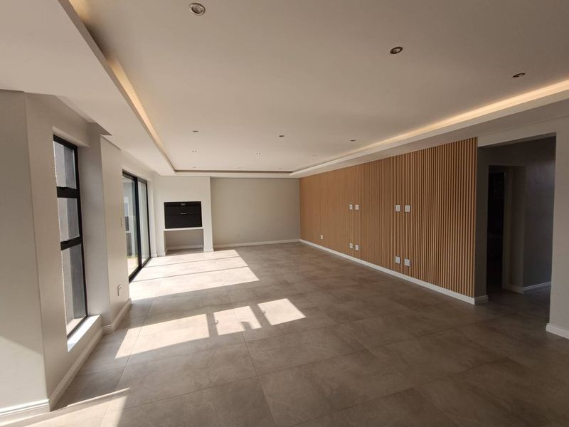 Spacious living area featuring modern timber slat wall paneling, recessed cove lighting, large format floor tiles, and a built-in fireplace with sliding door access.