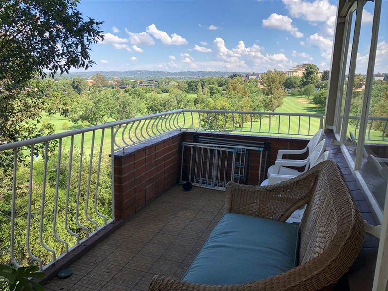 A balcony featuring a metal balustrade and brick wall, offering expansive views over the surrounding green landscape.