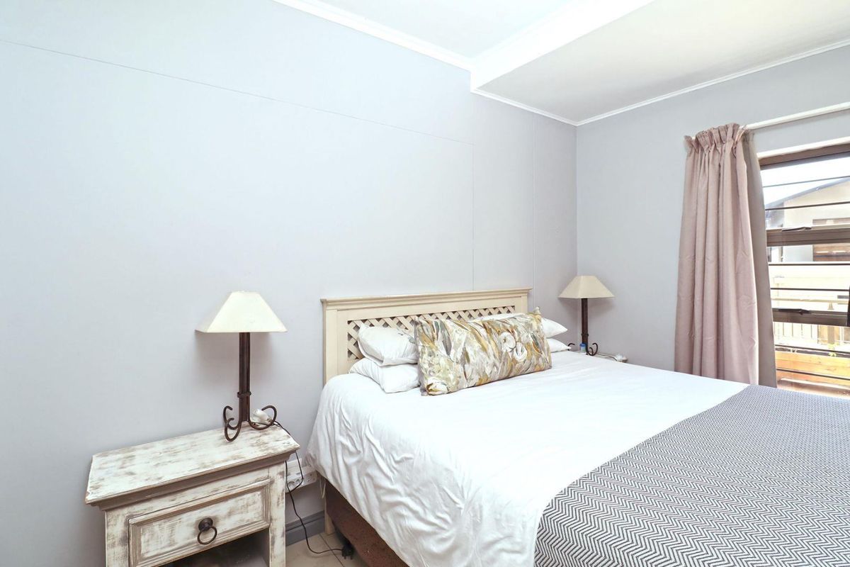 A well-lit bedroom featuring neutral wall tones, tiled flooring, and a window with curtain treatments.