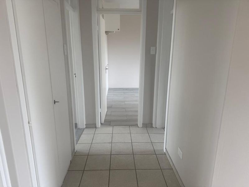 A bright, empty hallway featuring neutral tiled flooring and built-in cupboard storage, leading into an adjacent room.