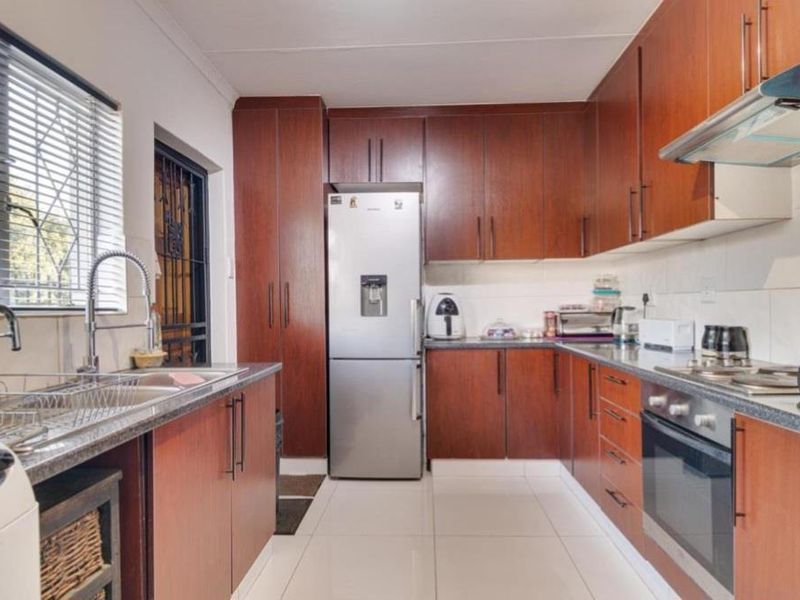 A functional kitchen featuring dark wood cabinetry, granite countertops, built-in oven, hob, extractor fan, and tiled flooring with a window overlooking the exterior.